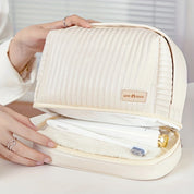 Borsa da toilette beige trapuntata con cerniera, contenente spazzolino e asciugamano. Design elegante, ideale per viaggi e organizzazione bagno.