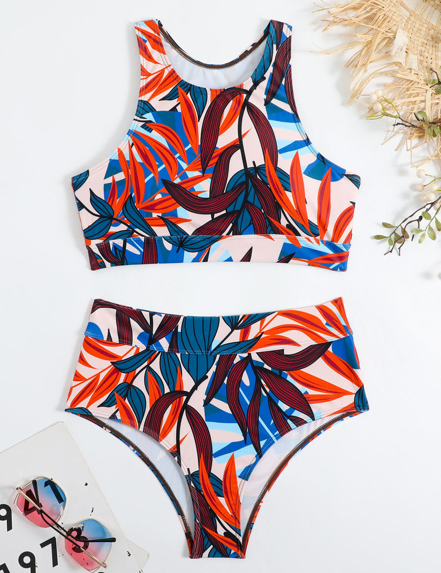 Costume da bagno donna a due pezzi con stampa tropicale colorata, top sportivo e slip a vita alta, occhiali da sole e cappello di paglia sullo sfondo.