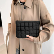 Donna con cappotto beige tiene una borsa trapuntata nera. Accessorio moda elegante, perfetto per l'autunno. Stile casual chic.
