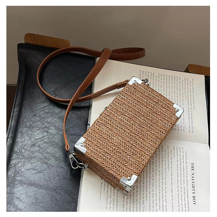 Borsa a tracolla in rattan intrecciato su sedia nera, design rettangolare, dettagli in metallo argentato, stile boho chic, moda donna.
