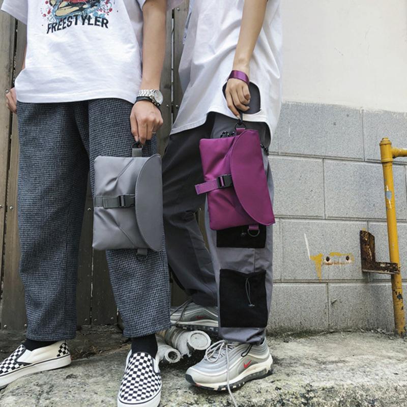 Due persone con pantaloni casual e scarpe sportive, tengono borse a mano moderne, una grigia e una viola. Stile urbano, moda streetwear.