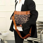 Borsa a tracolla leopardata con dettagli in pelle marrone, indossata da una persona in abito nero. Accessorio moda elegante e trendy.