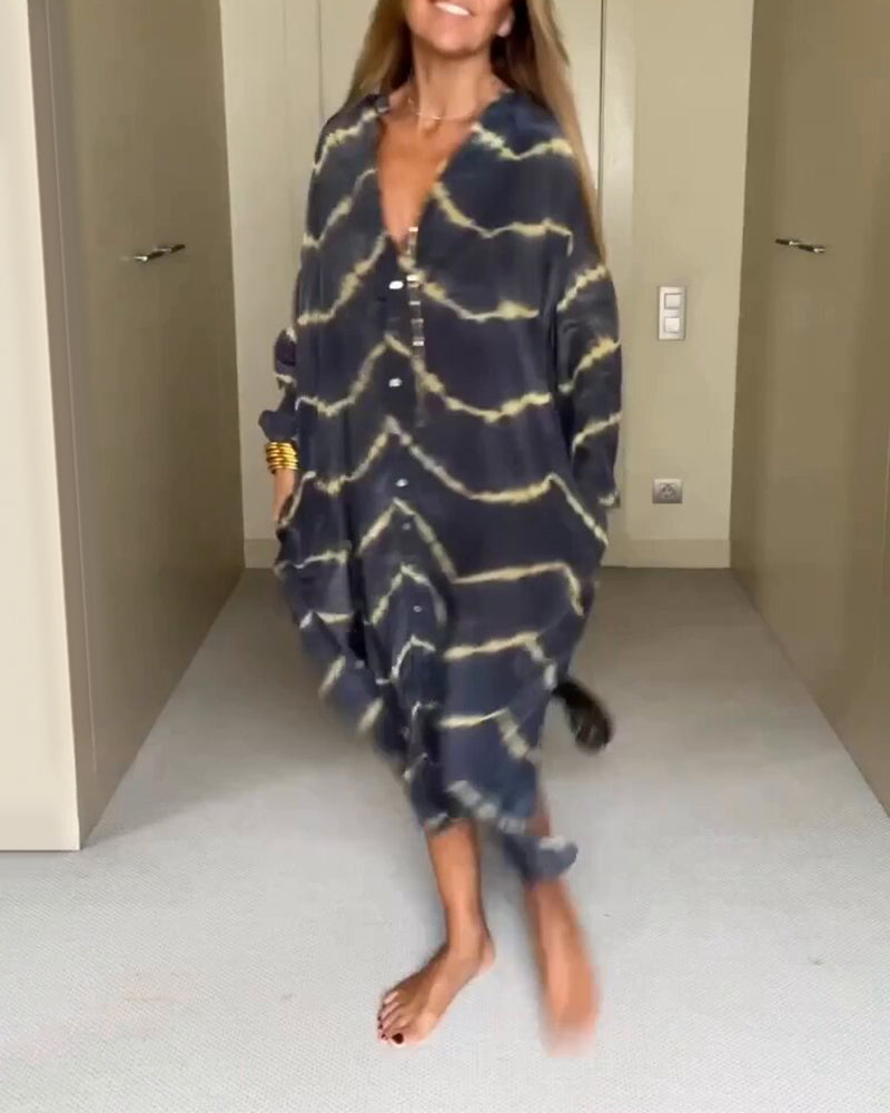 Donna che indossa un abito lungo a righe tie-dye blu e gialle, con bottoni e maniche lunghe, in piedi su un pavimento chiaro. Moda casual elegante.