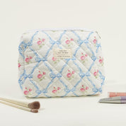 Astuccio cosmetico trapuntato con motivo floreale rosa e fiocchi blu, zip superiore. Include pennelli trucco e tubetti cosmetici.