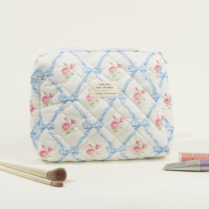 Astuccio cosmetico trapuntato con motivo floreale rosa e fiocchi blu, zip superiore. Include pennelli trucco e tubetti cosmetici.
