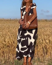 Donna in abito lungo bianco e nero con borsa marrone in un campo di grano. Moda estiva, abbigliamento casual, accessori eleganti.