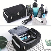 Borsa da toilette nera con zip, contenente prodotti per la cura personale e rasoio elettrico, su sfondo bianco. Accessori da viaggio uomo.