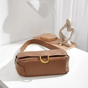 Borsa a tracolla in pelle marrone con chiusura dorata su tavolo bianco, lampada moderna e decorazione artistica. Accessorio moda elegante.