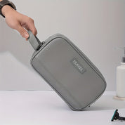 Mano che tiene un elegante beauty case da viaggio grigio, design compatto e moderno, ideale per organizzare accessori personali.