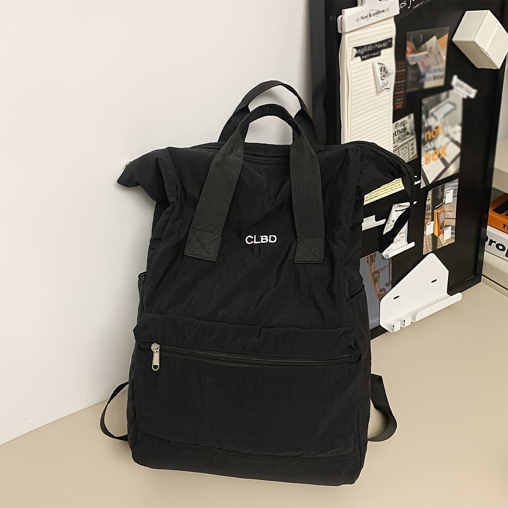 Zaino nero CLBD su scrivania, con tasca frontale con zip e manici superiori. Design moderno, ideale per scuola o lavoro. Accessori ufficio sullo sfondo.