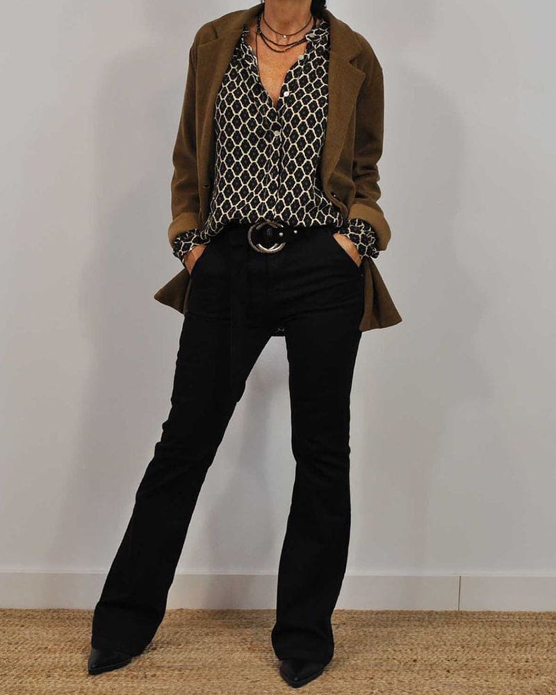 Donna in abbigliamento autunnale: blazer marrone, camicia a fantasia geometrica, pantaloni neri a zampa, stivali a punta. Moda casual chic.