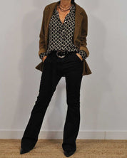 Donna in abbigliamento autunnale: blazer marrone, camicia a fantasia geometrica, pantaloni neri a zampa, stivali a punta. Moda casual chic.