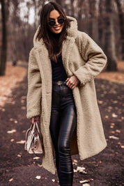 Donna con cappotto teddy beige, occhiali da sole e borsa elegante, passeggia in un parco autunnale. Moda invernale, stile casual chic.