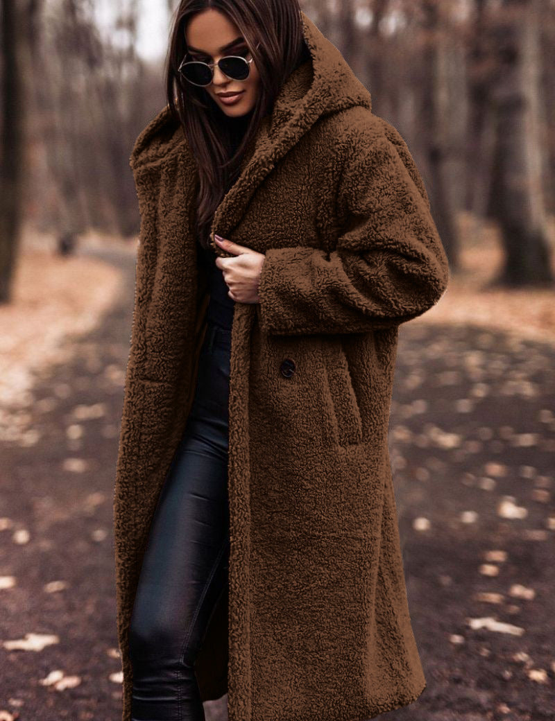 Donna con cappotto teddy marrone, occhiali da sole, pantaloni in pelle nera, in un parco autunnale. Moda invernale, stile casual chic.