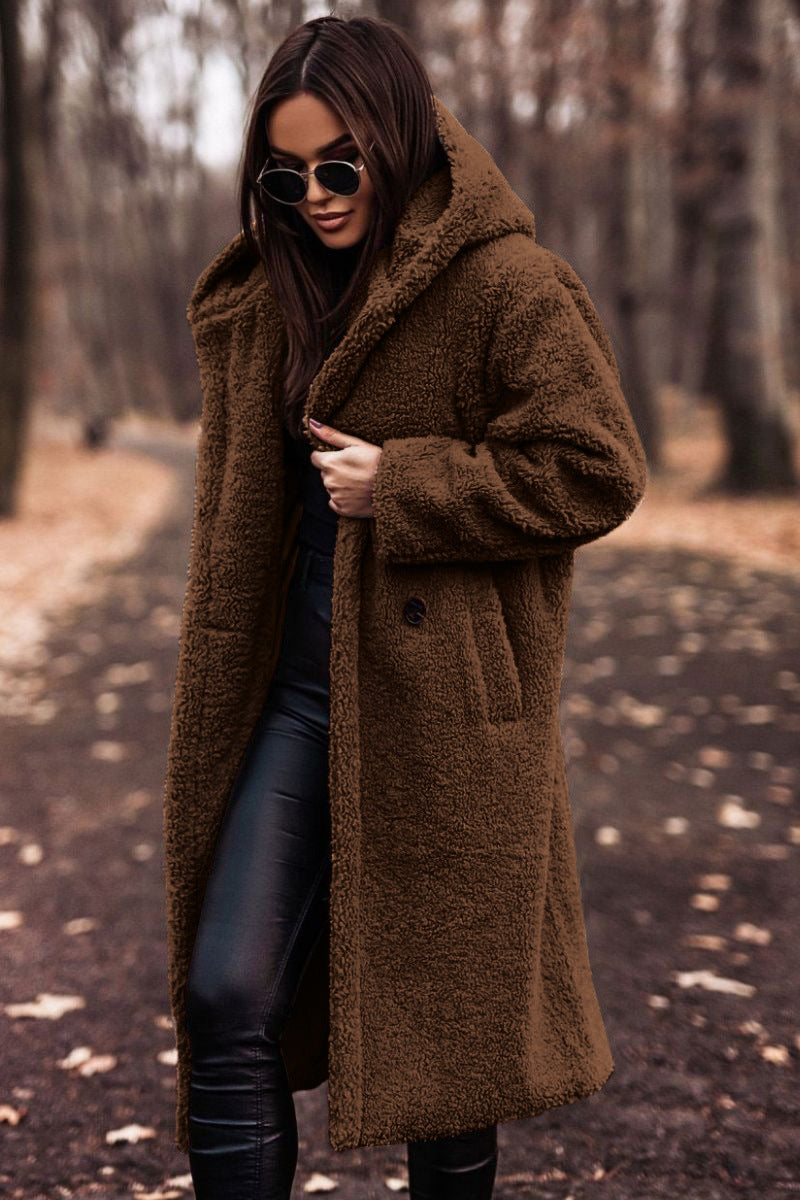 Donna con cappotto teddy marrone, occhiali da sole, pantaloni in pelle nera, in un parco autunnale. Moda invernale, stile casual chic.
