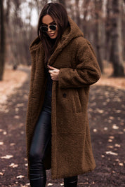 Donna con cappotto teddy marrone, occhiali da sole, pantaloni in pelle nera, in un parco autunnale. Moda invernale, stile casual chic.