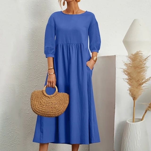 Donna con abito blu a maniche lunghe, borsa di paglia intrecciata, sfondo bianco minimalista, decorazione pampas. Moda estiva elegante.