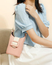 Donna con borsa a tracolla rosa, design elegante con fibbia, indossa camicetta azzurra e gonna bianca. Accessorio moda femminile chic.