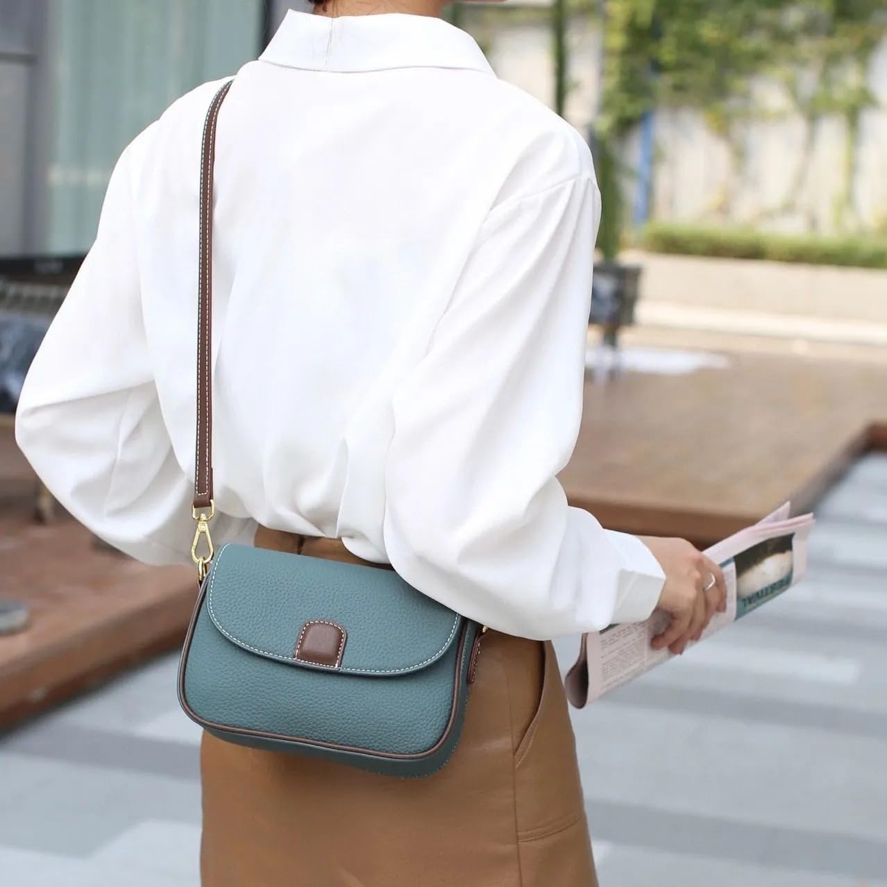 Donna con camicia bianca e borsa a tracolla verde, elegante e moderna, tiene una rivista. Moda femminile, accessori di tendenza, stile urbano.