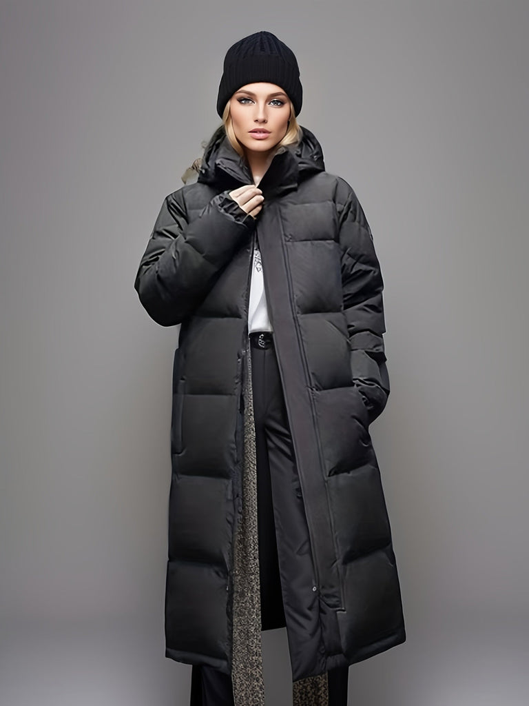 Cappotto lungo imbottito nero da donna, con cappuccio, indossato con pantaloni eleganti e maglione bianco. Stile invernale moderno e caldo.