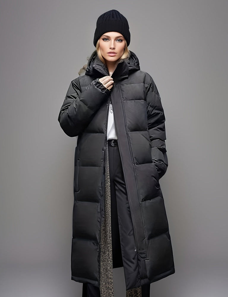Cappotto lungo imbottito nero da donna, con cappuccio, indossato con pantaloni eleganti e maglione bianco. Stile invernale moderno e caldo.