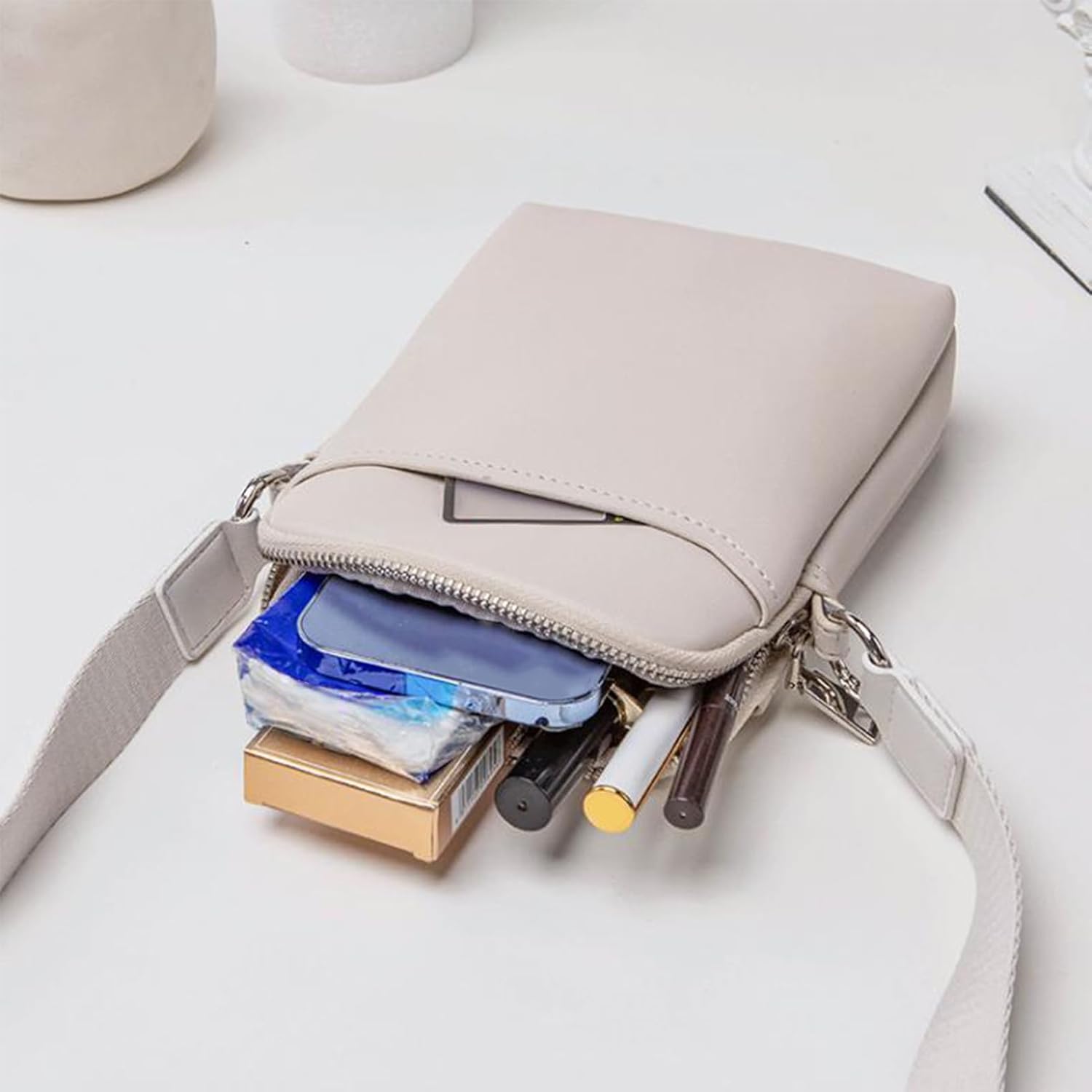 Borsa a tracolla beige aperta con trucchi e accessori visibili, design elegante e compatto, ideale per moda femminile e organizzazione quotidiana.