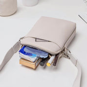 Borsa a tracolla beige aperta con trucchi e accessori visibili, design elegante e compatto, ideale per moda femminile e organizzazione quotidiana.