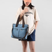 Donna con borsa a tracolla in tela blu, tasche frontali, manici marroni, indossa cappello arancione e maglietta beige. Moda casual estiva.