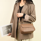 Donna con borsa a tracolla marrone in pelle, indossa blazer beige e tiene una foto. Elegante accessorio moda femminile, stile casual chic.