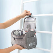 Borsa da toilette grigia appesa, con scomparti aperti e accessori da viaggio. Design compatto, ideale per organizzare prodotti personali.