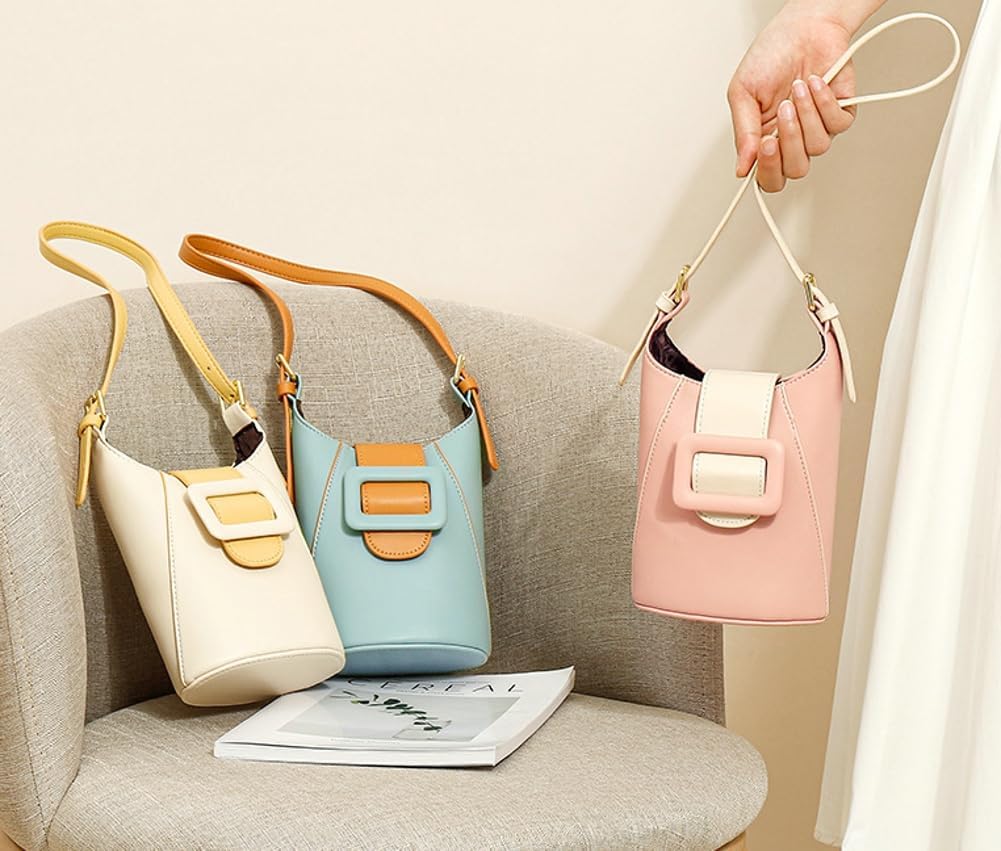 Tre borse a secchiello in pelle color crema, azzurro e rosa con fibbia decorativa, su sedia beige. Accessori moda eleganti per donna.