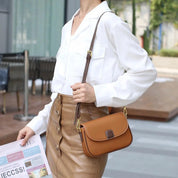 Donna con camicia bianca e gonna marrone, tiene una borsa a tracolla in pelle marrone chiaro. Accessorio moda elegante e casual.
