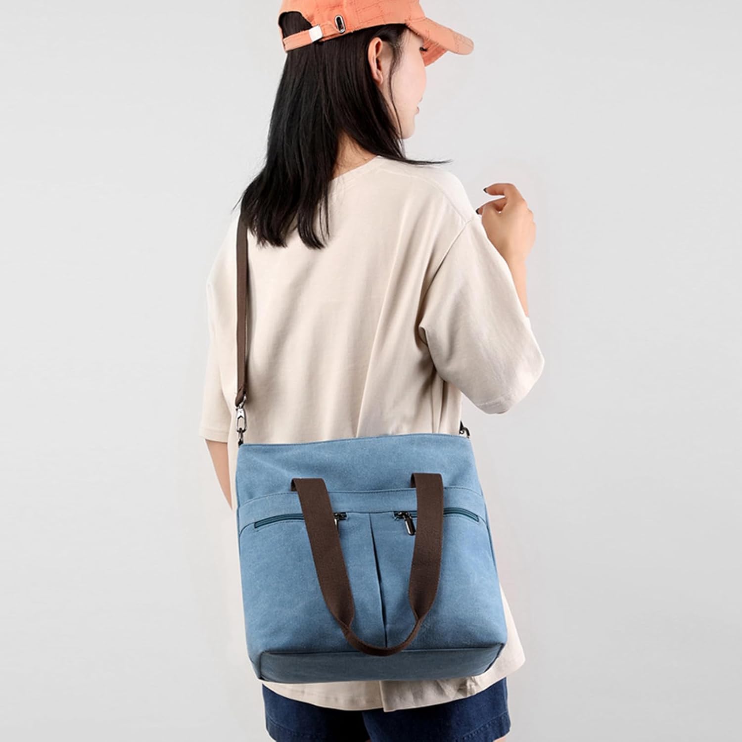 Donna con borsa a tracolla in tela blu, manici marroni, indossa cappello arancione e maglietta beige. Accessorio moda casual e pratico.