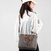 Donna con borsa a tracolla in tela grigia, design casual, manici marroni, abbigliamento bianco, cappello beige. Accessorio moda donna.
