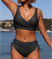Donna in bikini nero a vita alta su spiaggia, costume da bagno estivo, moda mare, top incrociato, accessori, sfondo marino, look elegante.