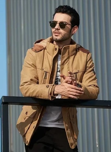 Uomo con giacca beige casual, occhiali da sole, appoggiato a una ringhiera. Moda maschile autunnale, stile urbano, abbigliamento outdoor.