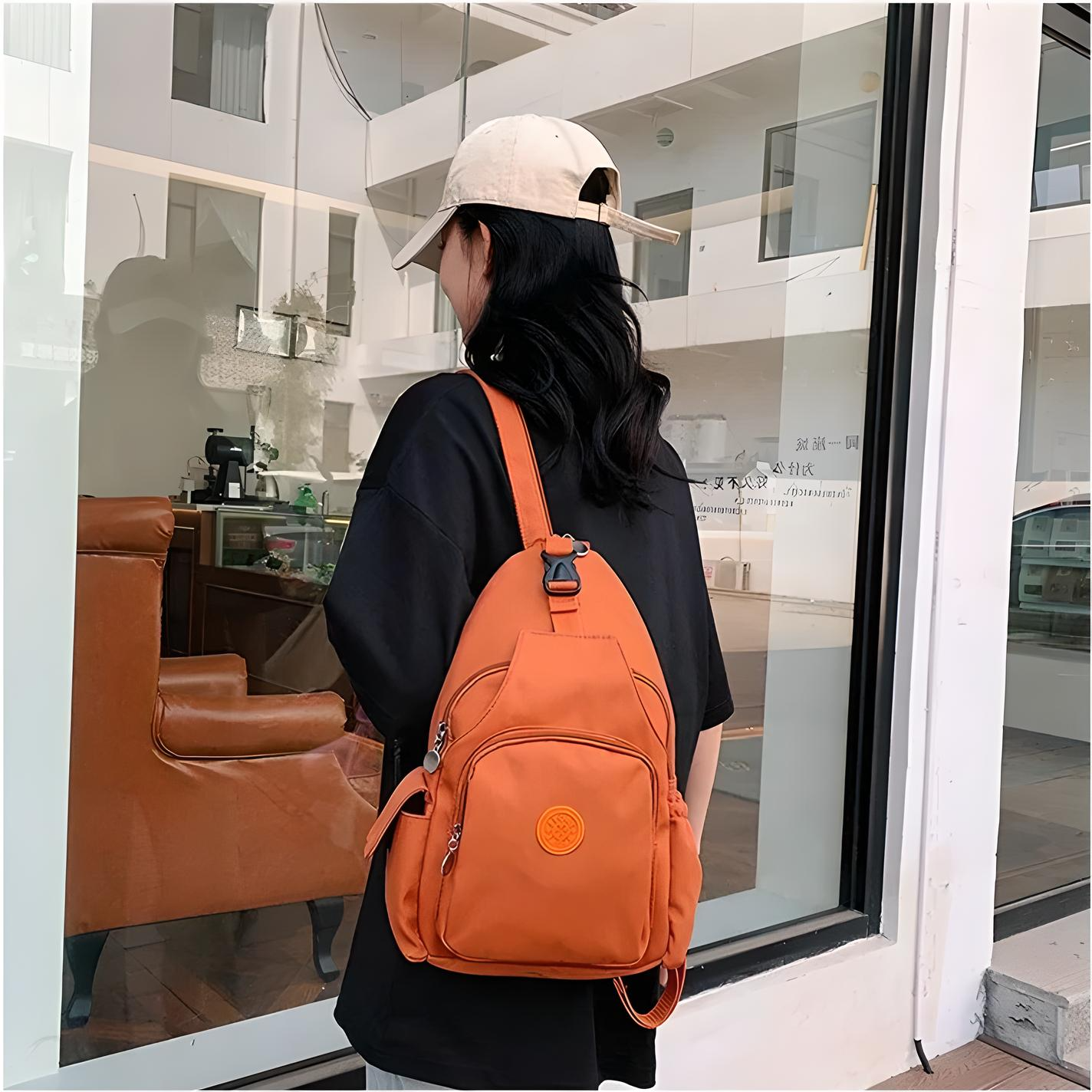 Zaino arancione casual indossato da una persona con cappellino bianco e maglietta nera, davanti a una vetrina. Accessorio moda urbano.