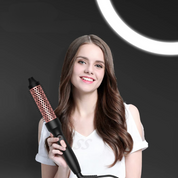 Donna sorridente con capelli lunghi e ondulati, tiene una spazzola arricciacapelli elettrica nera e rosa, sfondo nero, luce circolare.