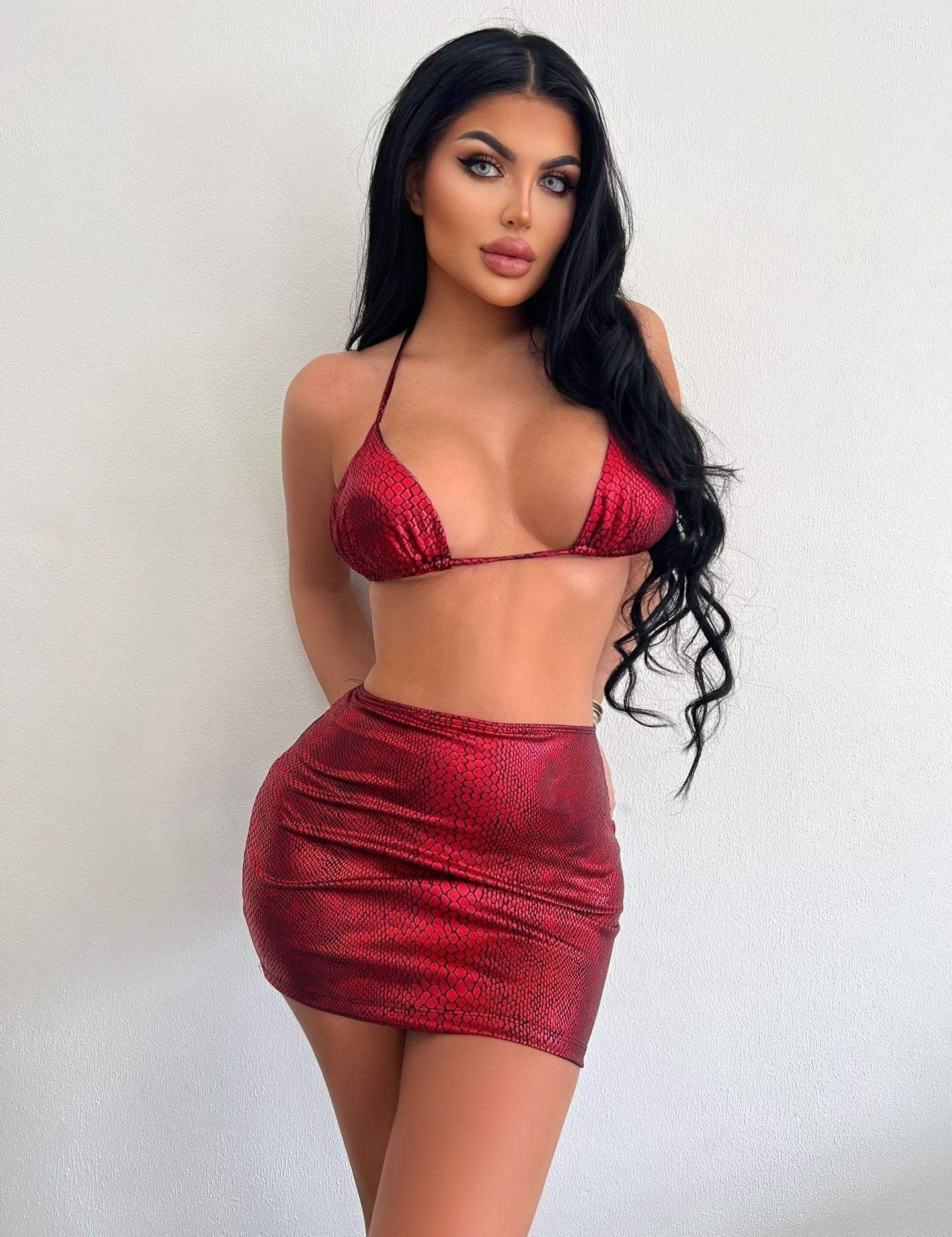 Modella in bikini rosso lucido con stampa serpente, posa contro sfondo bianco. Moda estiva, abbigliamento da spiaggia, tendenze 2023.
