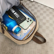 Zaino aperto con smartphone, bottiglia d'acqua blu, libro e astuccio nero su pavimento grigio. Accessori viaggio, tecnologia, organizzazione.
