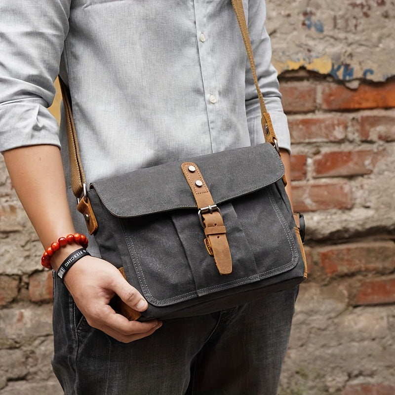 Borsa a tracolla in tela grigia con chiusura in pelle marrone, indossata da uomo in camicia grigia. Accessorio moda casual, ideale per uso quotidiano.