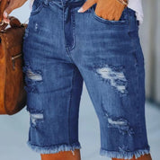 Shorts di jeans strappati da donna, blu, con dettagli sfrangiati. Moda casual estiva, stile urbano. Donna con borsa marrone.