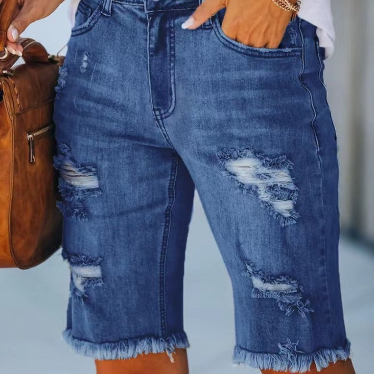 Shorts di jeans strappati da donna, blu, con dettagli sfrangiati. Moda casual estiva, stile urbano. Donna con borsa marrone.