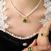 Collana di perle con ciondolo verde su abito nero con pizzo bianco, anello coordinato. Gioielli eleganti, moda donna, accessori di lusso.
