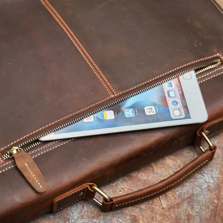 Borsa in pelle marrone con cerniera aperta, mostra smartphone all'interno. Elegante accessorio moda uomo, ideale per lavoro e viaggi.