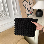Cuscino nero lavorato a maglia su divano beige, decorazione murale con cane stilizzato, lampada moderna; arredamento elegante e accogliente.