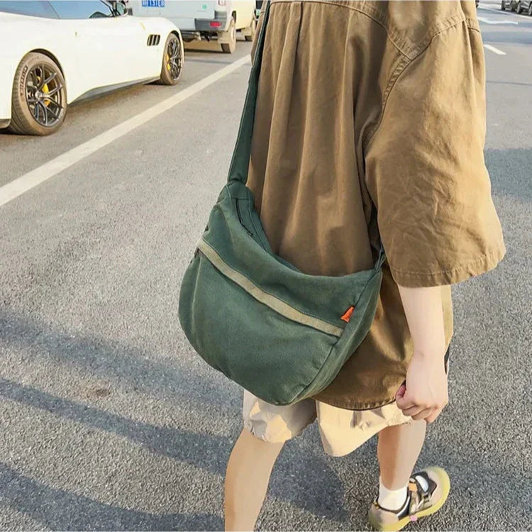 Uomo con borsa a tracolla verde in tessuto, strada urbana, auto sportive sullo sfondo. Accessorio moda casual, stile quotidiano.