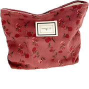 Astuccio cosmetico in tessuto rosa con motivo floreale, chiusura a zip, ideale per trucco e accessori. Design elegante e pratico per viaggio.