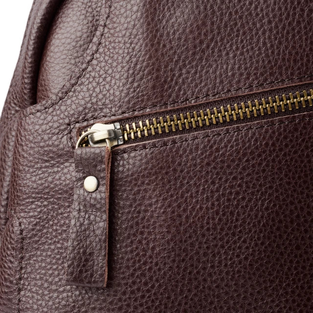 Zaino in pelle marrone con texture granulosa, cerniera in metallo dorato e tiralampo in pelle. Accessorio moda elegante e resistente.