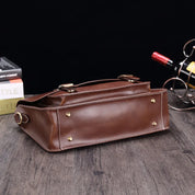 Borsa a tracolla in pelle marrone su tavolo di legno, con dettagli in metallo dorato. Elegante accessorio moda, perfetto per uomo e donna.